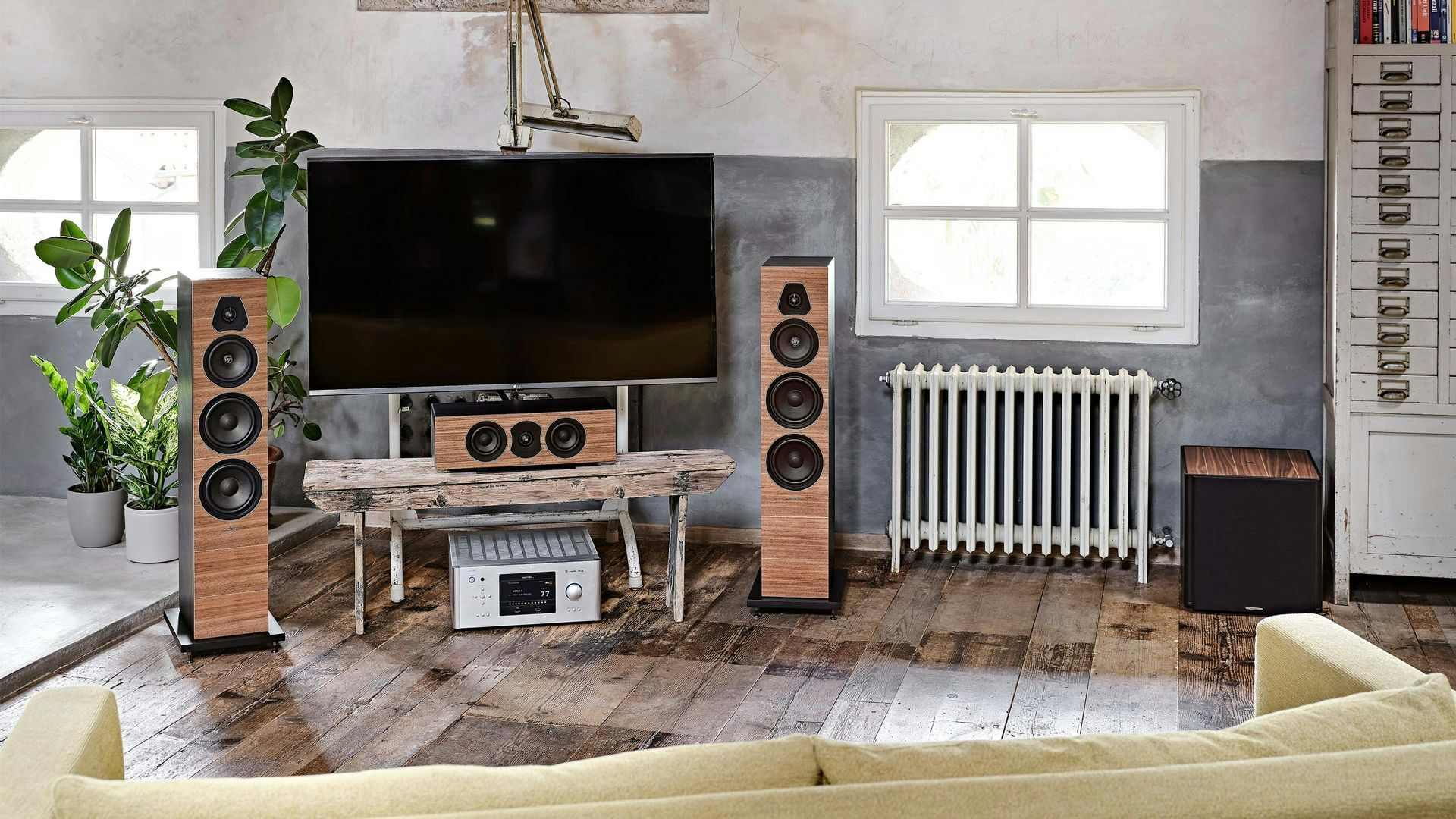 Sonus faber Gravis III subwoofer in walnut wood, complementing Olympica Nova speakers in a home audio setup with a TV.