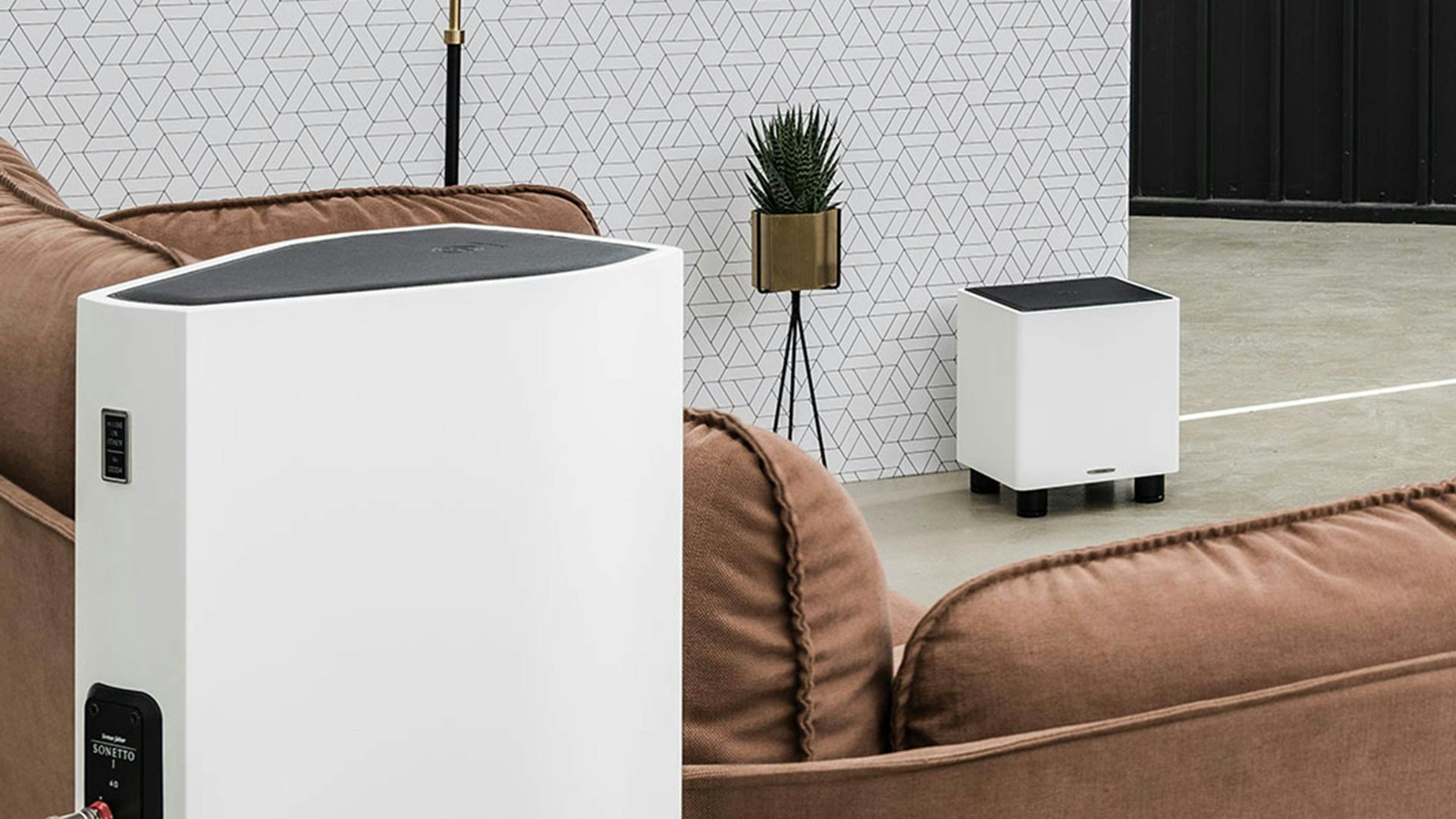 A matte white Sonus faber Gravis I subwoofer, accompanied by a matching Lumina bookshelf speaker in a home audio room